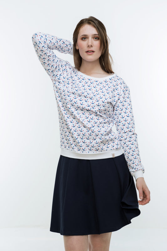 Eine junge Frau mit langen Haaren. Sie trägt ein weißes Sweatshirt, das mit blauen Ankern bedruckt ist, die an den Ankerhaken je ein Herzchen haben. Das Sweatshirt hat lange Ärmel und einen breiten, runden Ausschnitt. Als Abschluss an den Ärmeln, am Bund und am Hals hat es weiße Bündchen. 
Ansicht frontal, ein Arm hinter dem Kopf.