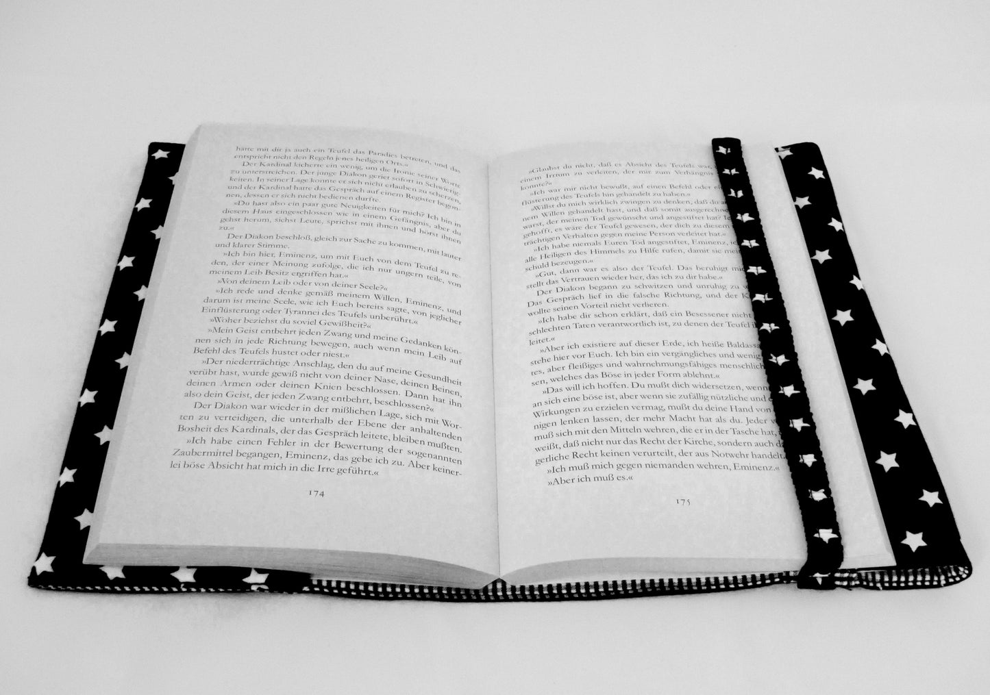 Das aufgeschlagene Buch in der schwarzen Buchhülle mit den weißen Sternen. Der bezogene Gummi hält die Seiten auf der rechten Seite fest und fungiert auch als Lesezeichen.