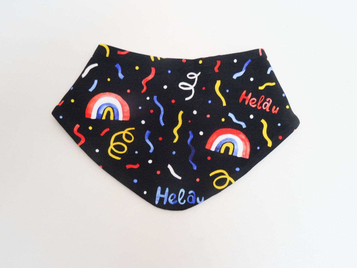 Halstuch für Babys und kleine Kinder schwarz mit buntem Schriftzug Helau, Konfetti, Luftschlangen und Regenbögen. Ansicht liegend frontal.