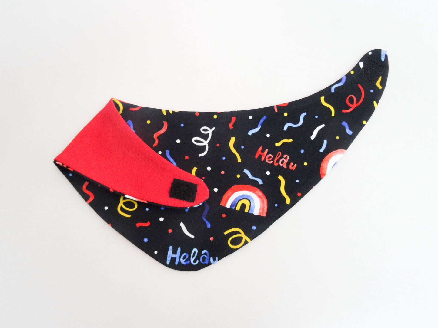 Halstuch für Babys und kleine Kinder schwarz mit buntem Schriftzug Helau, Konfetti, Luftschlangen und Regenbögen. Ansicht aufgeklappt mit umgeschlagener Seite. Die rote Rückseite ist sichtbar.