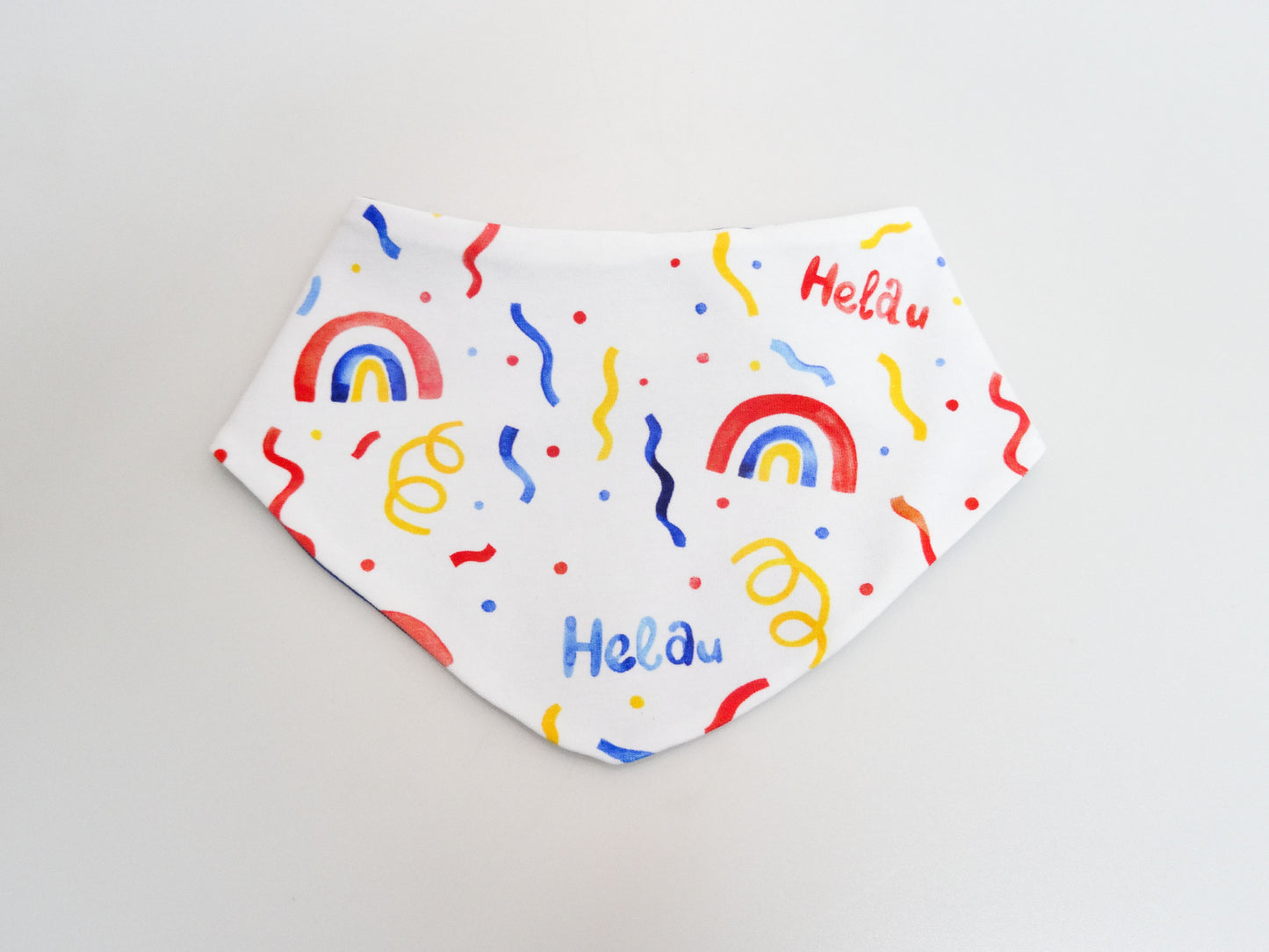 Halstuch für Babys und kleine Kinder weiss mit buntem Schriftzug Helau, Konfetti, Luftschlangen und Regenbögen. Ansicht liegend frontal.
