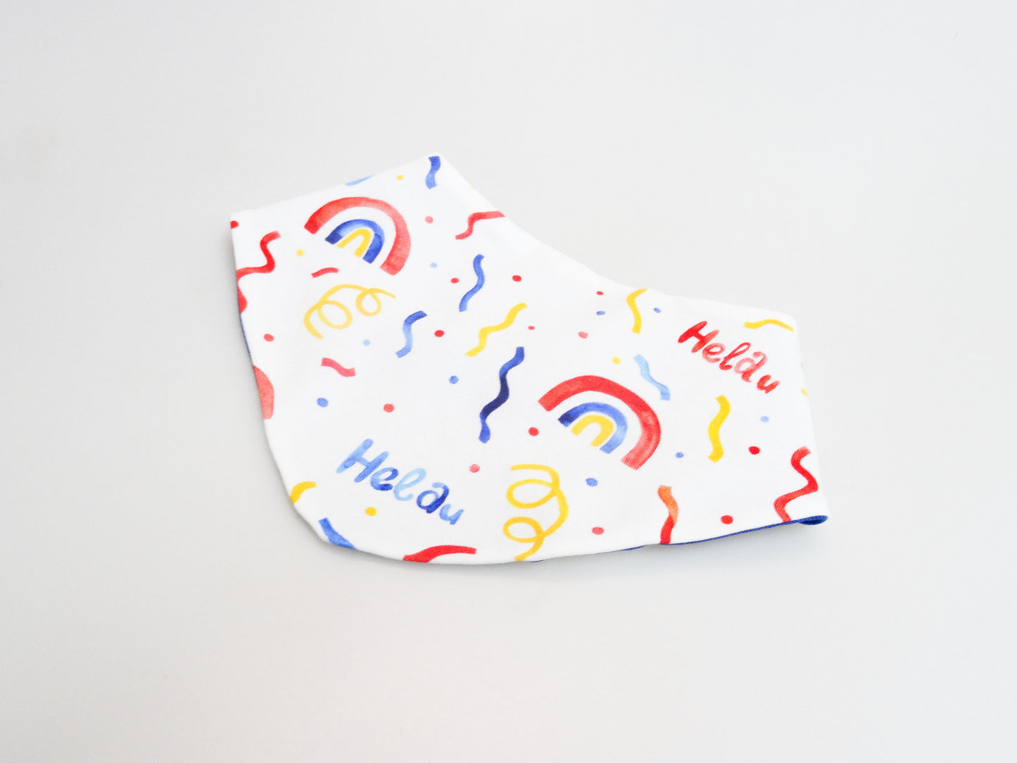 Halstuch für Babys und kleine Kinder weiss mit buntem Schriftzug Helau, Konfetti, Luftschlangen und Regenbögen. Ansicht liegend seitlich.