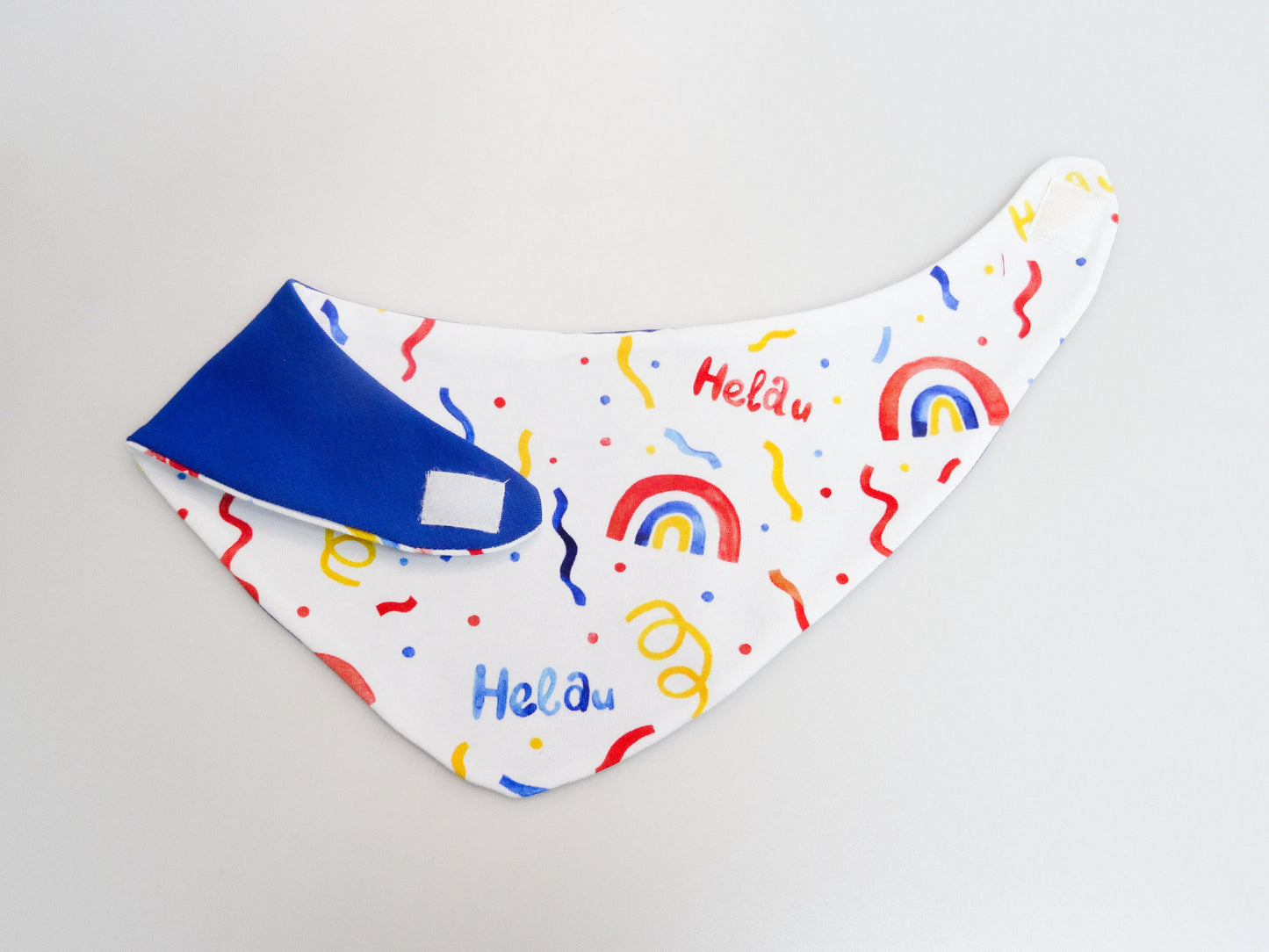 Halstuch für Babys und kleine Kinder weiss mit buntem Schriftzug Helau, Konfetti, Luftschlangen und Regenbögen. Ansicht aufgeklappt mit umgeschlagener Seite. Die blaue Rückseite ist sichtbar.