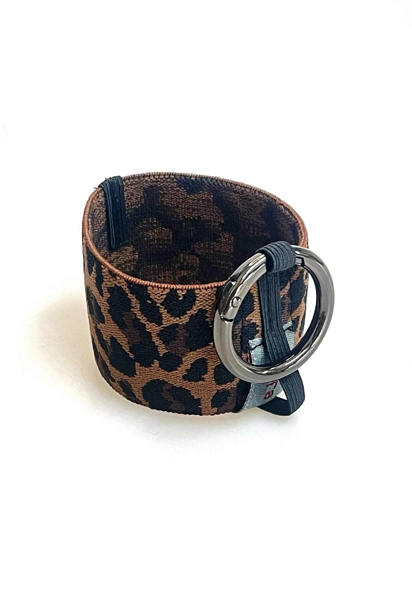 Ein Becherhalter aus einem breiten Gummiband mit Leoparden Muster. Er hat einem runden, gunmetal farbenen Karabinerhaken. Das Gummiband ist zu einem Kreis zusammengenäht. Der Karabiner ist an einem schmalen Gummiband befestigt, das unten um das breite Gummiband herum geht.
