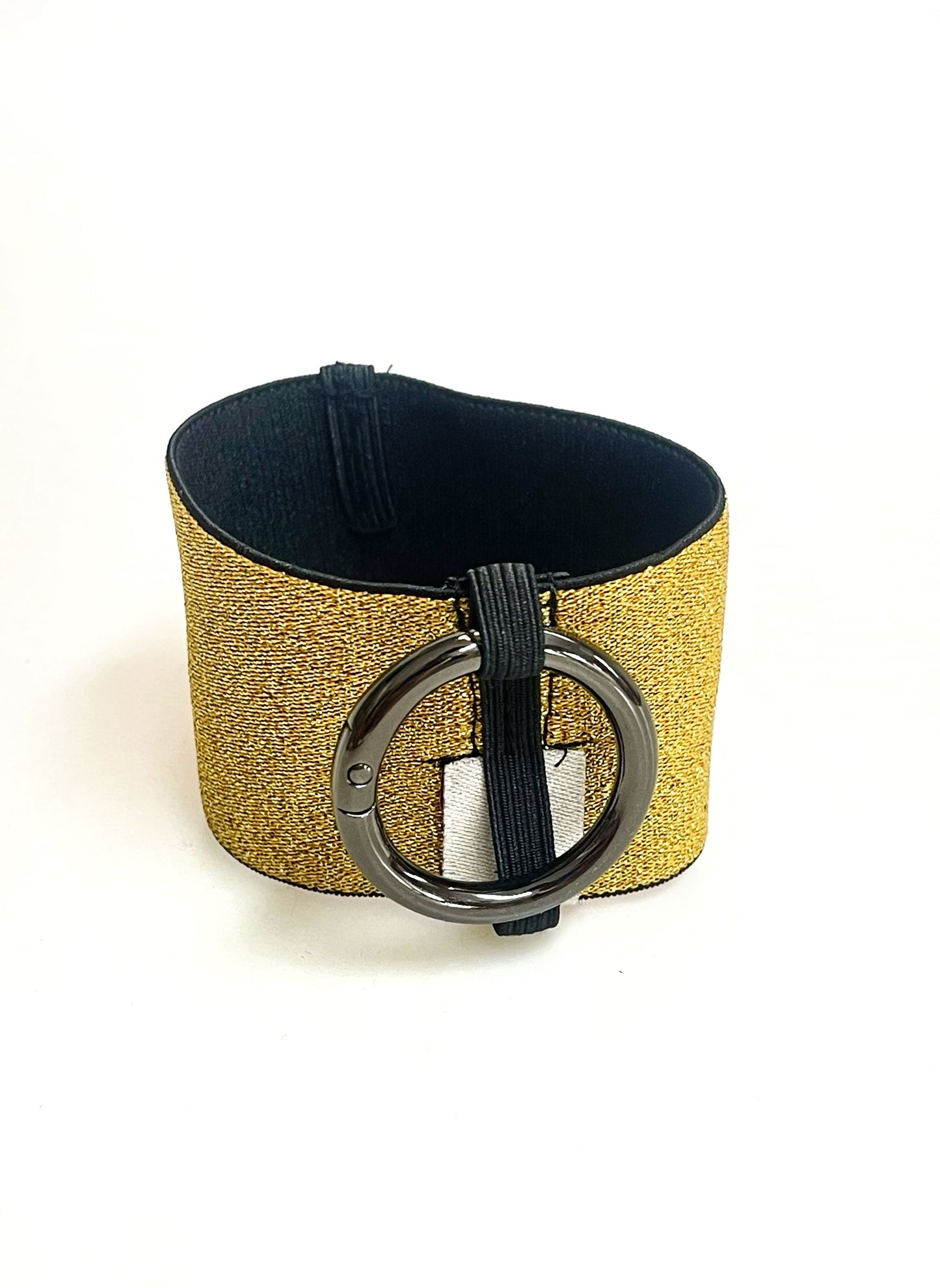 Ein Becherhalter aus einem gold glitzernden, breiten Gummiband, innen schwarz, mit einem runden, gunmetal farbenen Karabinerhaken. Das Gummiband ist zu einem Kreis zusammengenäht. Der Karabiner ist an einem Schmalen Gummiband befestigt, das unten um das breite Gummiband herum geht.