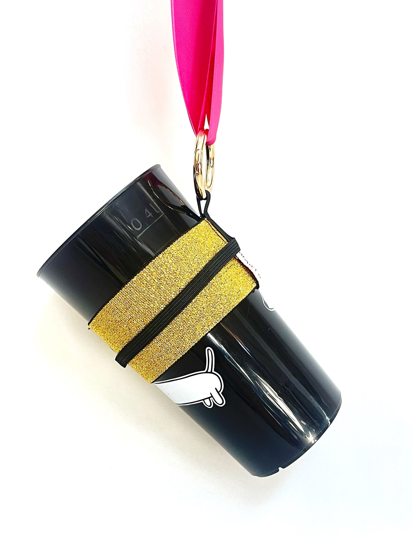 Ein Becher steckt im goldenen Becherhalter. Das schmale, schwarze Gummiband ist hochgeklappt und liegt auf einer Seite des breiten Becherhalter. Der Karabinerhaken hängt an einem pinken Band.