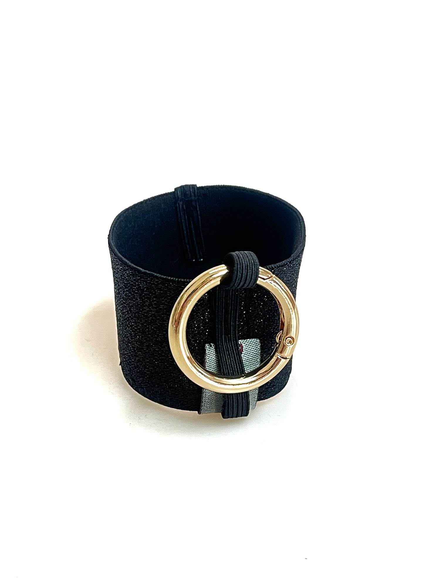 Ein Becherhalter aus einem schwarz glitzernden, breiten Gummiband, innen schwarz, mit einem runden, goldenen Karabinerhaken. Das Gummiband ist zu einem Kreis zusammengenäht. Der Karabiner ist an einem Schmalen Gummiband befestigt, das unten um das breite Gummiband herum geht.