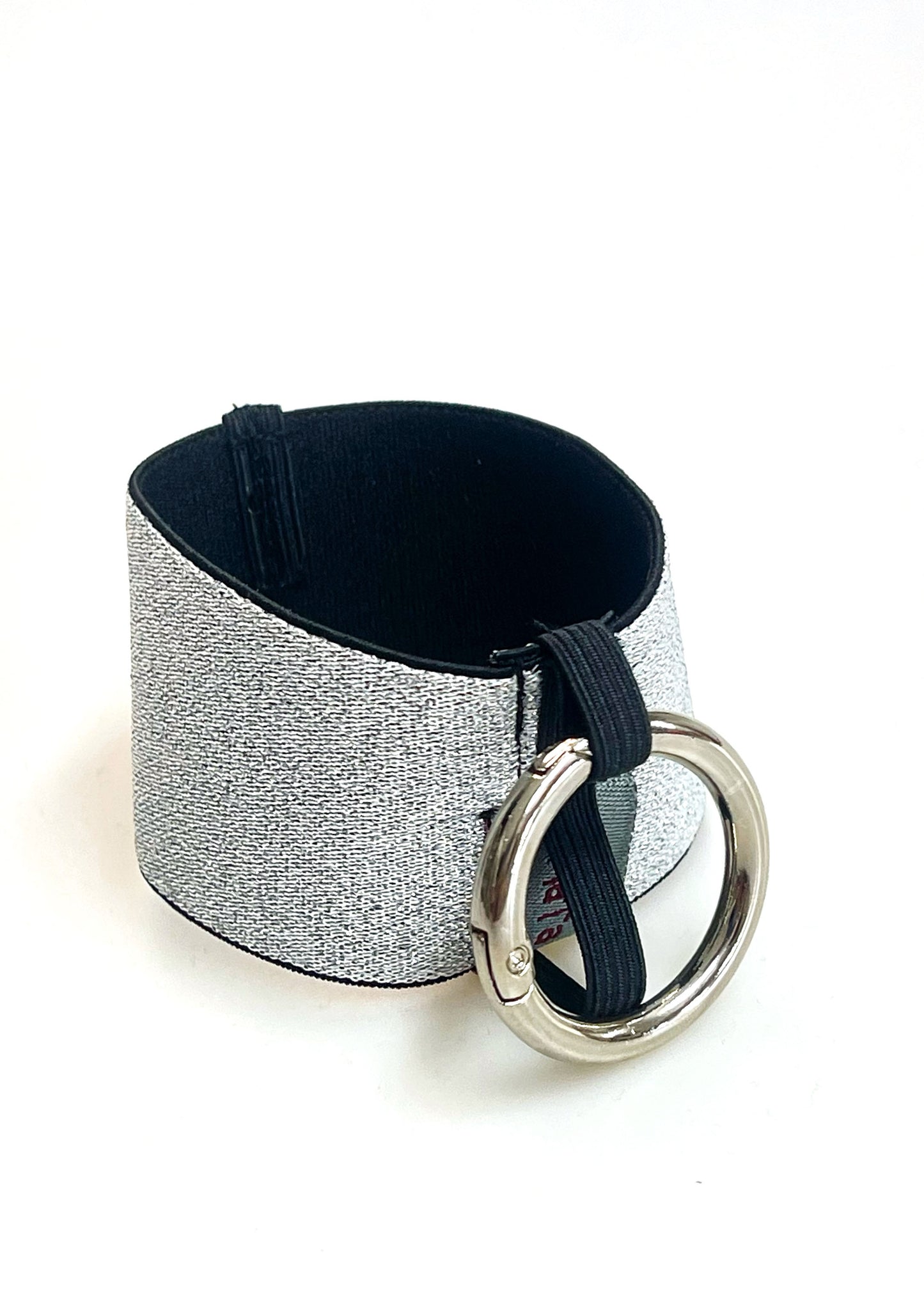 Ein Becherhalter aus einem silber glitzernden, breiten Gummiband, innen schwarz, mit einem runden, silbernen Karabinerhaken. Das Gummiband ist zu einem Kreis zusammengenäht. Der Karabiner ist an einem Schmalen Gummiband befestigt, das unten um das breite Gummiband herum geht.
