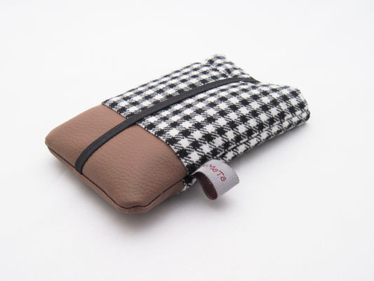 Eine Handytasche aus einem schwarz-weißen Wollstoff mit Pepita Muster oben und braunem Kunstleder unten. Die Tasche hat eine aufgesetzte Tasche aus dem Pepitastoff und ist mit schwarzem Gummiband geschlossen. 
Aufnahme seitlich von unten.