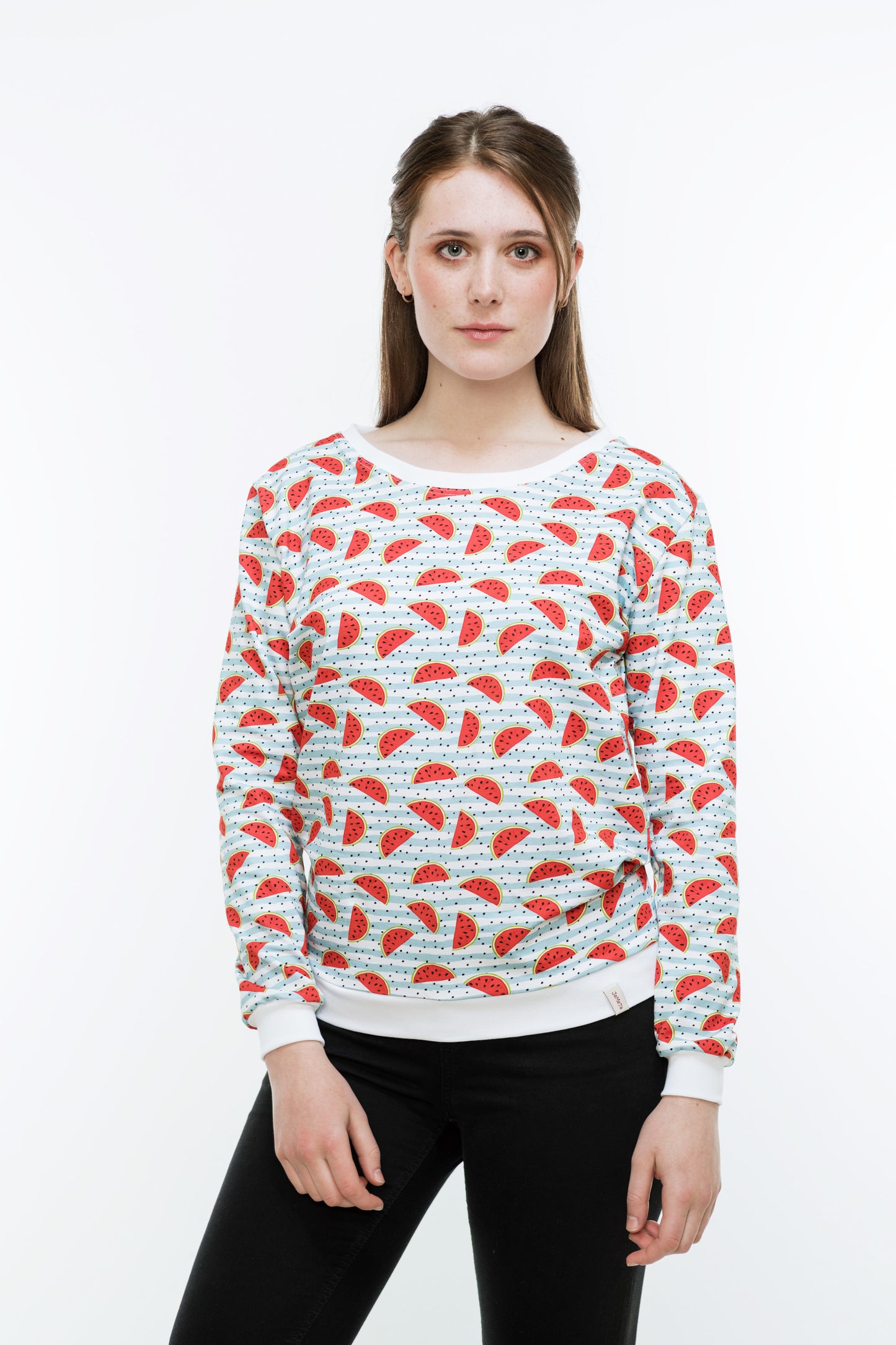 Junge Frau mit langen Haaren in einer engen, schwaren Hose und einem Sweatshirt mit Melonendruck. Es ist weiß und mit roten Wassermelonen und schwarzen Pünktchen auf hellblauen Streifen bedruckt ist. Der Pulli hat weiße Bündchen an Saum, Ärmeln und Halsausschnitt.
Der Halsausschnitt ist rund und etwas größer.