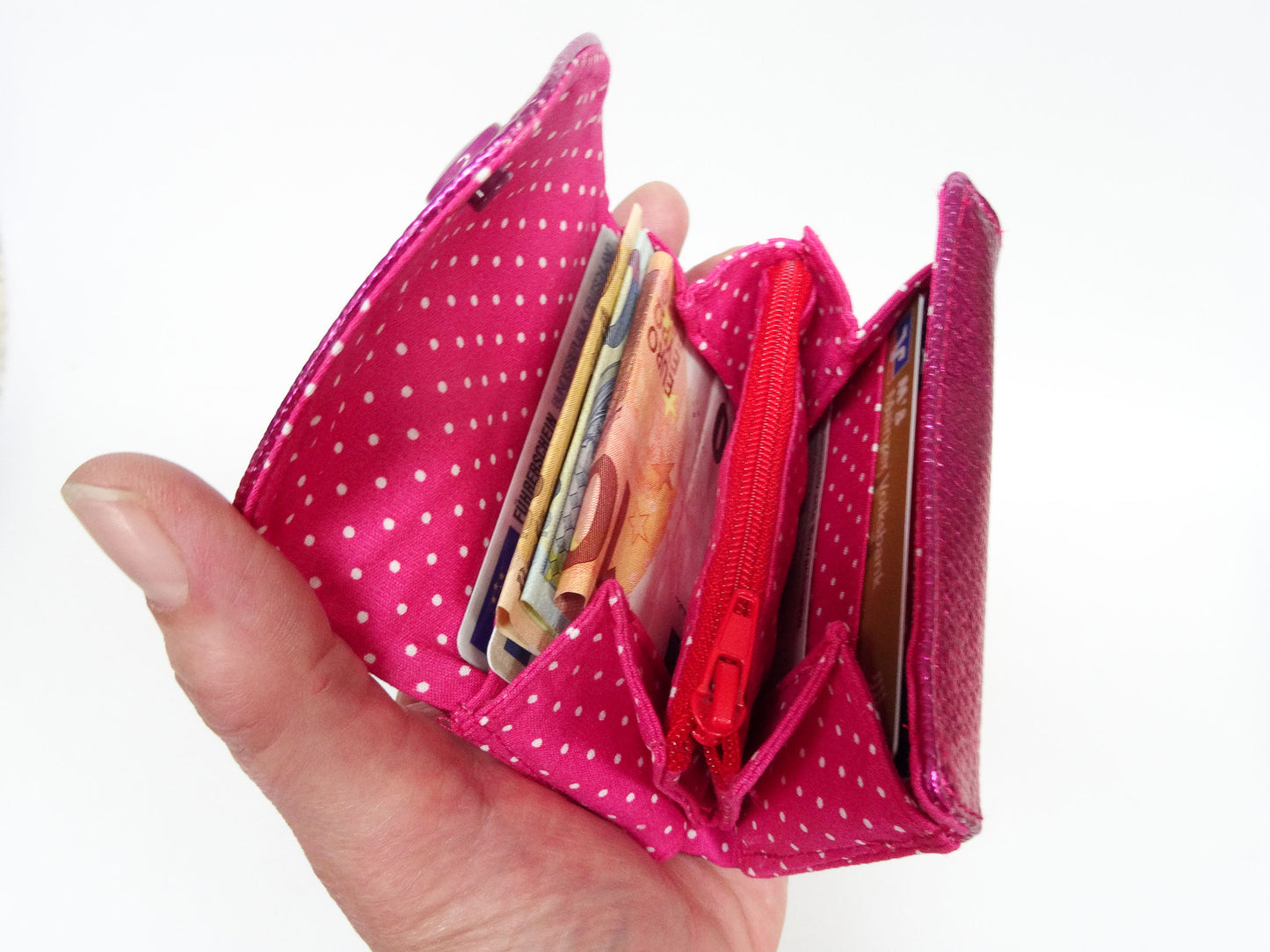 Die aufgeklappte pinke Börse gefüllt in einer Hand.