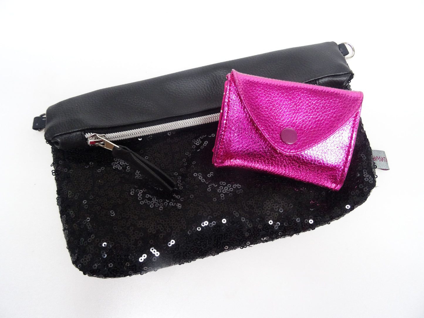 Die pinke Geldbörse auf einer kleinen, schwarzen Handtasche mit Pailletten liegend. Bild, um das Größenverhältnis zu zeigen.