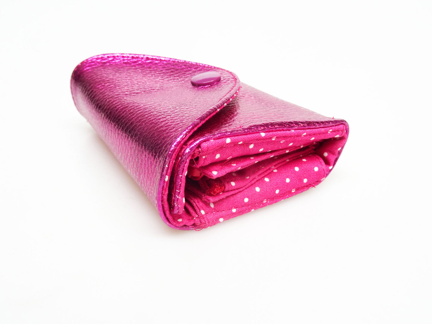 Kleine Geldbörse in metallic pink mit dreieckiger Klappe und pinkem Innenleben mit weißen Pünktchen. Das Innenleben ist an der Seite sichtbar. Aufnahme schräg von oben.