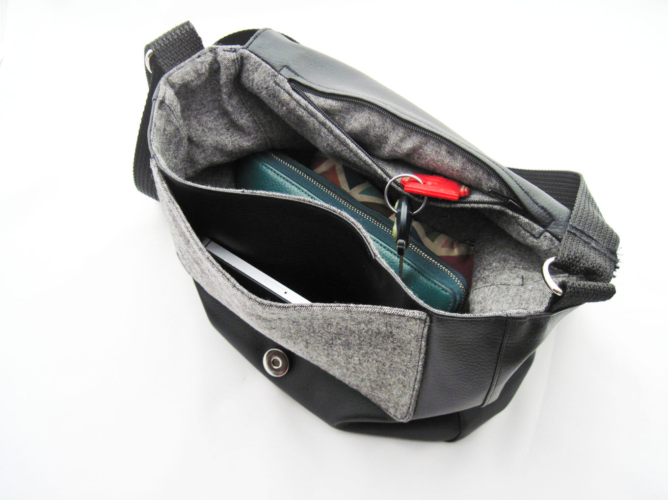 Innenansicht der Tasche. Sie hat ein Tweedfutter. Es gibt ein großes Fach, eine Innentasche mit Reißverschluss und eine aufgesetzte Tasche auf dem Vorderteil, in die ein Smartphone passt.