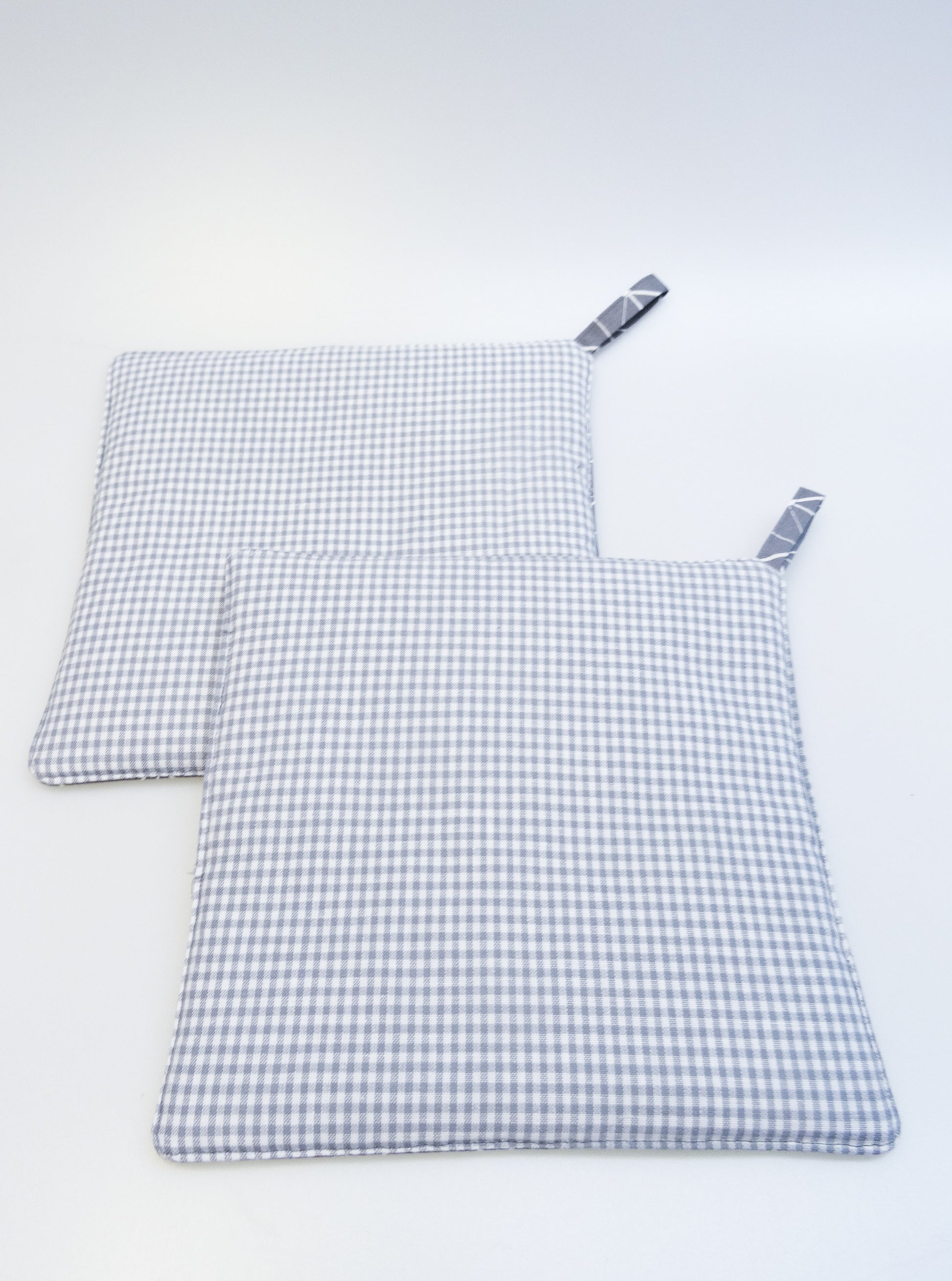 Die grauen Topflappen mit dem weißen Strichemuster, beide von der Seite mit dem Vichykaro.