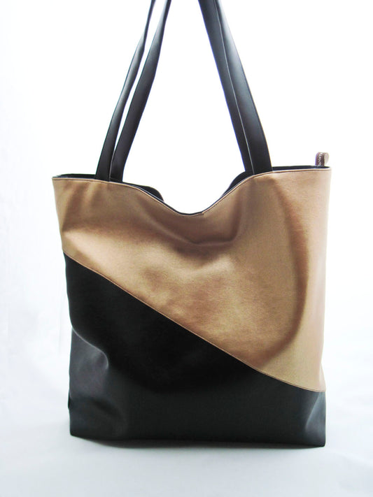 Ein Shopper aus Kunstleder vor einem weißen Hintergrund. Die Tasche ist diagonal geteilt. Der untere Teil und die Träger sind schwarz. Der oberer Teil ist gold. Die Tasche ist rechteckig und höher, als breit.