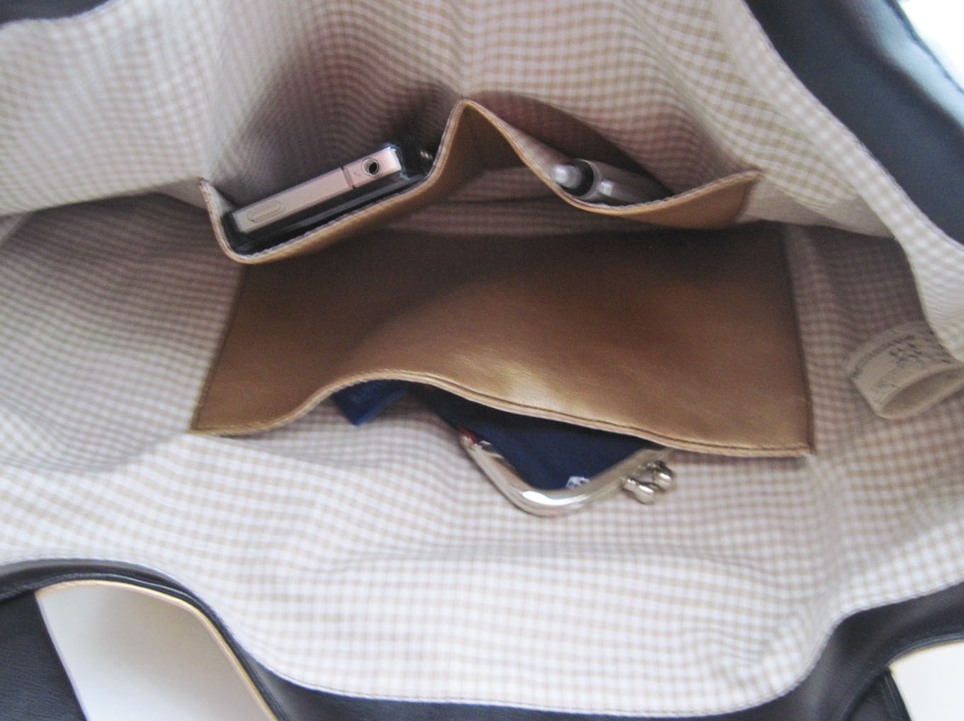 Innenansicht des Shoppers. Man sieht das Futter aus beige-weißem Vichykaro und dass die Tasche zwei aufgesetzte Innentaschen hat. In den Innentaschen stecken ein Handy, ein Portemonnaie und ein Kugelschreiber.