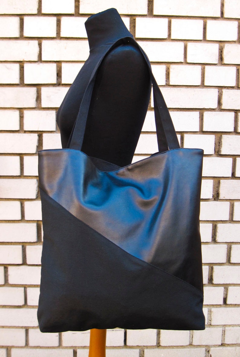 Der diagonal geteilte, schwarze Shopper auf der Schulter einer schwarzen Schneiderpuppe vor einer schwarz-weiß gemauerten Wand.