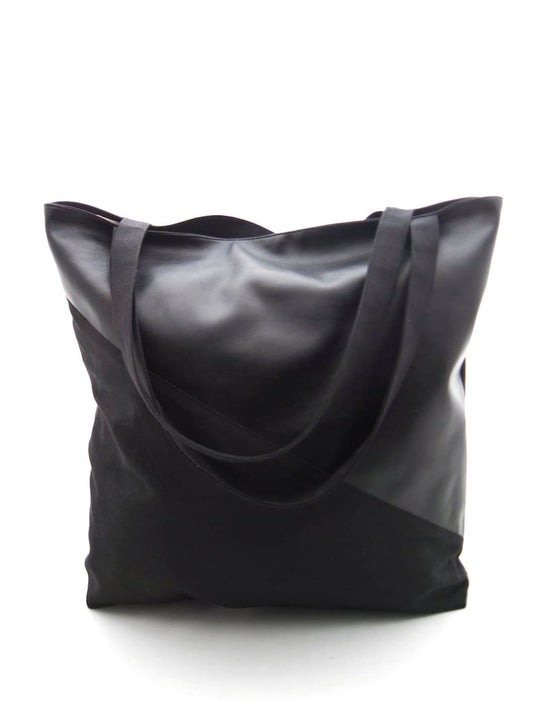 Ein Shopper aus Kunstleder und Canvas vor einem weißen Hintergrund. Die Tasche ist diagonal geteilt. Der untere Teil und die Träger sind aus schwarzem Canvas. Der oberer Teil ist aus schwarzem Kunstleder. Die Tasche ist rechteckig und höher, als breit.