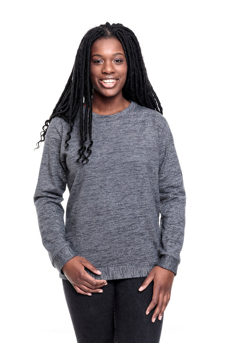 Eine junge Frau mit langen Braids. Sie trägt ein graues, meliertes Sweatshirt mit silbernen Lurexfäden. Das Sweatshirt ist ca. hüftlang, hat lange Ärmel und einen Runden Halsausschnitt. Als Abschluss an den Ärmeln, dem Bund und dem Hals hat der Pulli Bündchen aus dem gleich Stoff. 
Ansicht frontal.