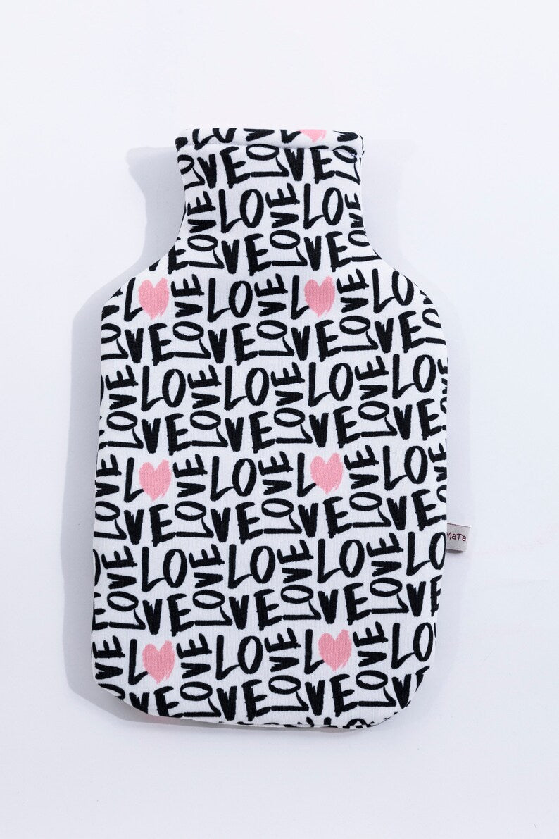 Eine liegende, weiße Wärmflaschenhülle mit schwarzem "Love" Schriftzug und rosa Herzen. Ansicht vorne, von oben.