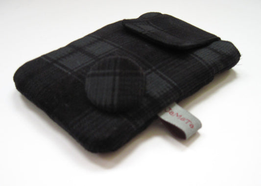Eine Handytasche aus schwarz-grau kariertem Feincord. Die Tasche hat eine Klappe zum Verschließen und unten rechts einen Button aus dem Cordstoff. 
Aufnahme seitlich von unten.