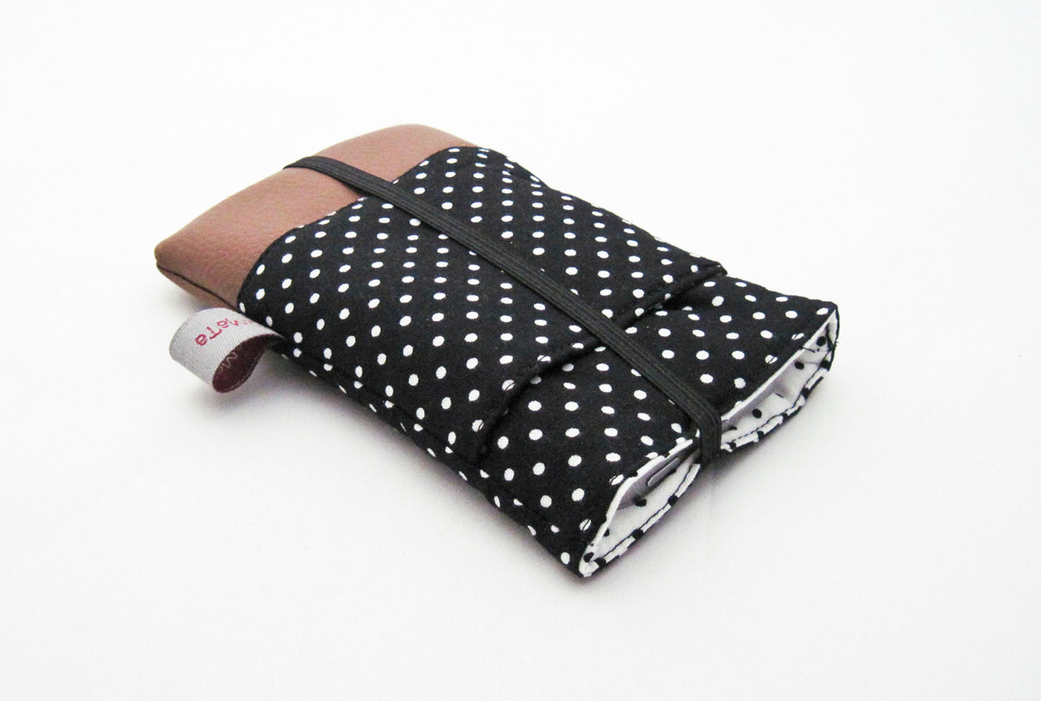 Eine schwarze Handytasche mit weißen Pünktchen. Die Tasche hat eine zusätzliche, aufgesetzte Tasche, einen Boden aus braunem Kunstleder und ein weißes Futter mit schwarzen Pünktchen. Sie wird mit schwarzem Gummiband verschlossen.
