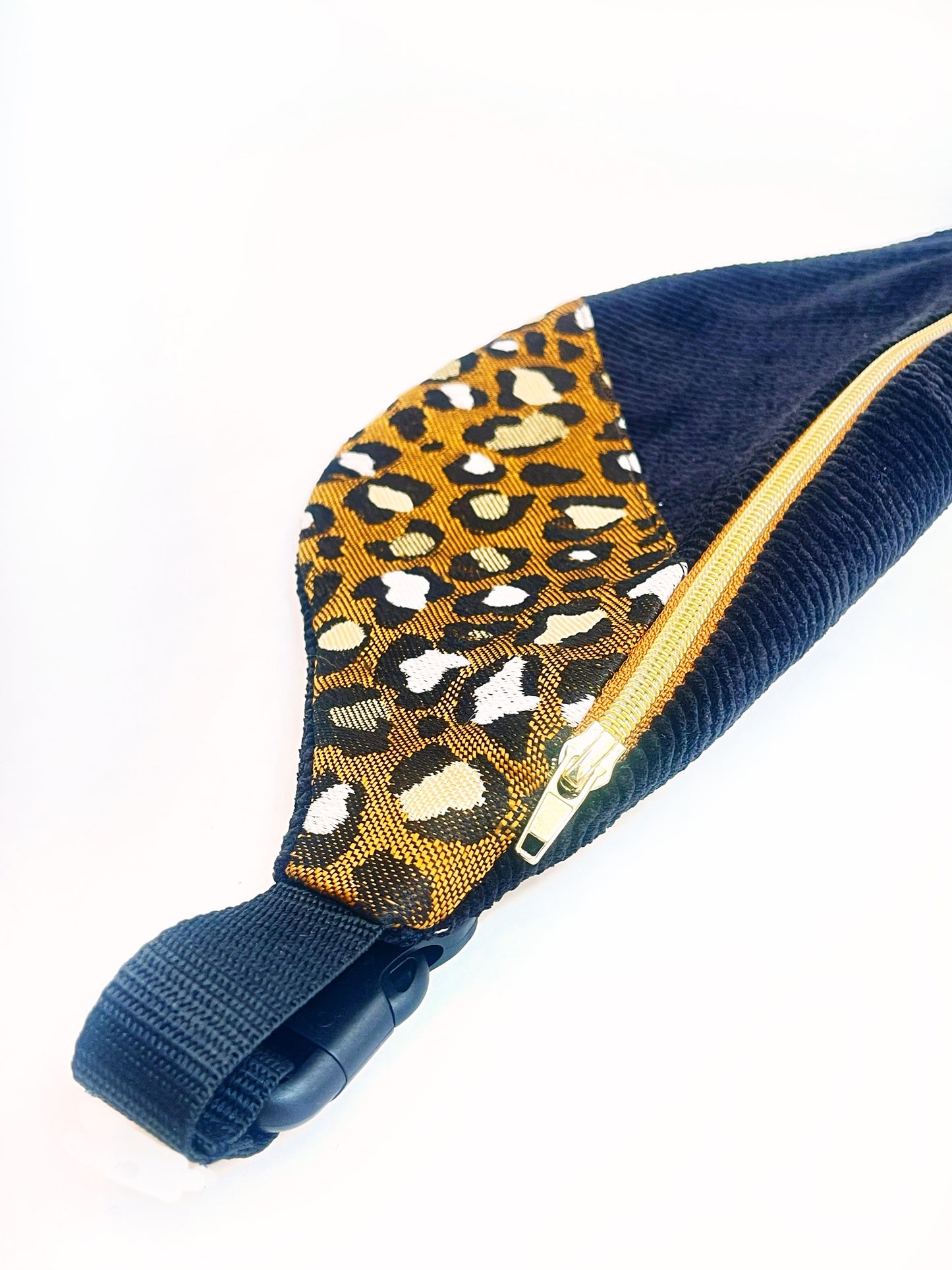 Detailansicht der geteilten Bauchtasche von oben. Man sieht gut den teil mit bdem Leopardendruck und den gildenen Reißverschluss. Auch der Deckel und die Steckschnalle sind zu sehen. 