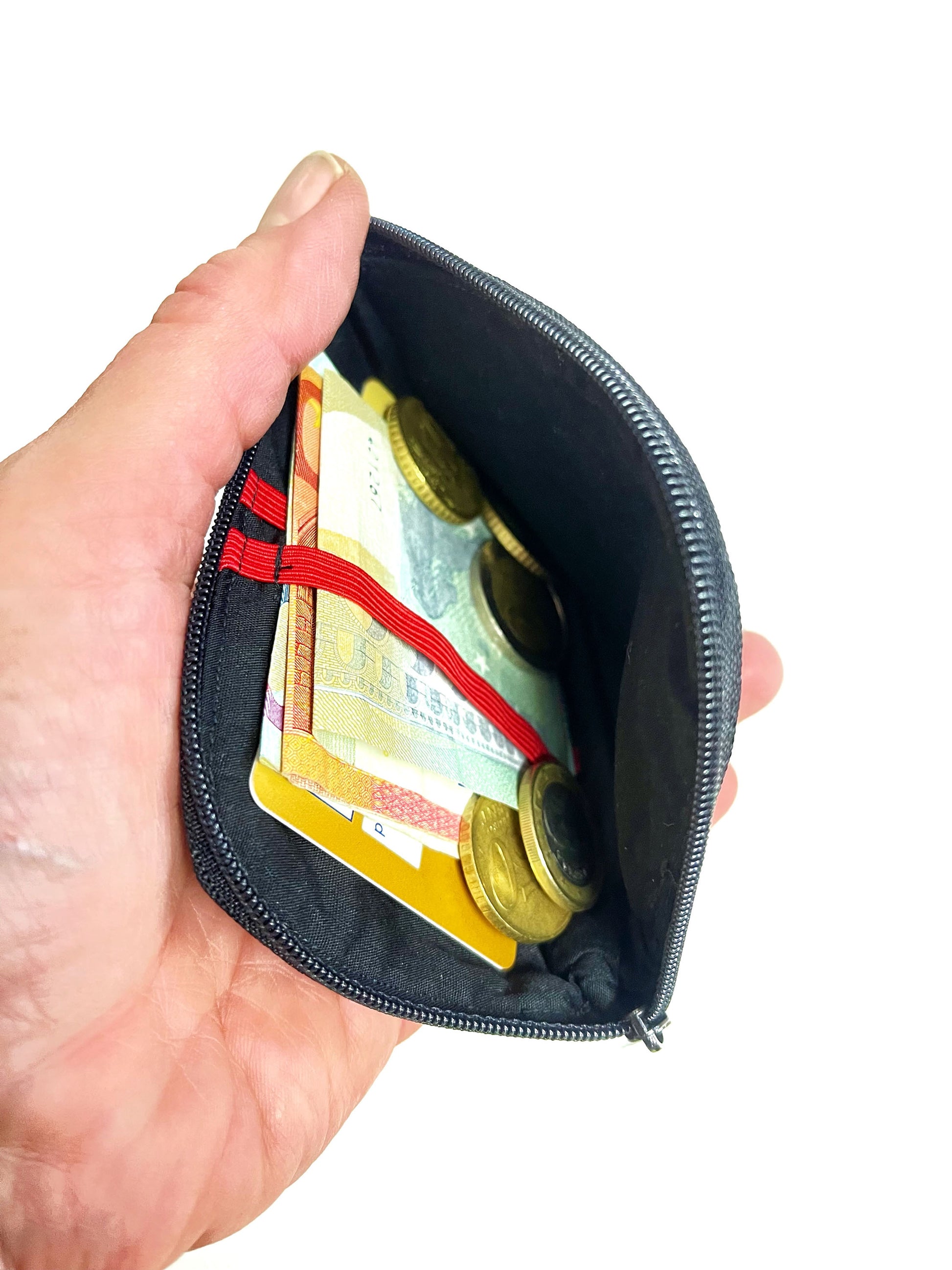 Eine Hand hält die geöffente Börse. Man schaut auf das schwarze Innenfutter und die roten Gummbänder. In den Bändern stecken Geldscheine und eine EC-Karte. Kleingeld liegt daneben.  
