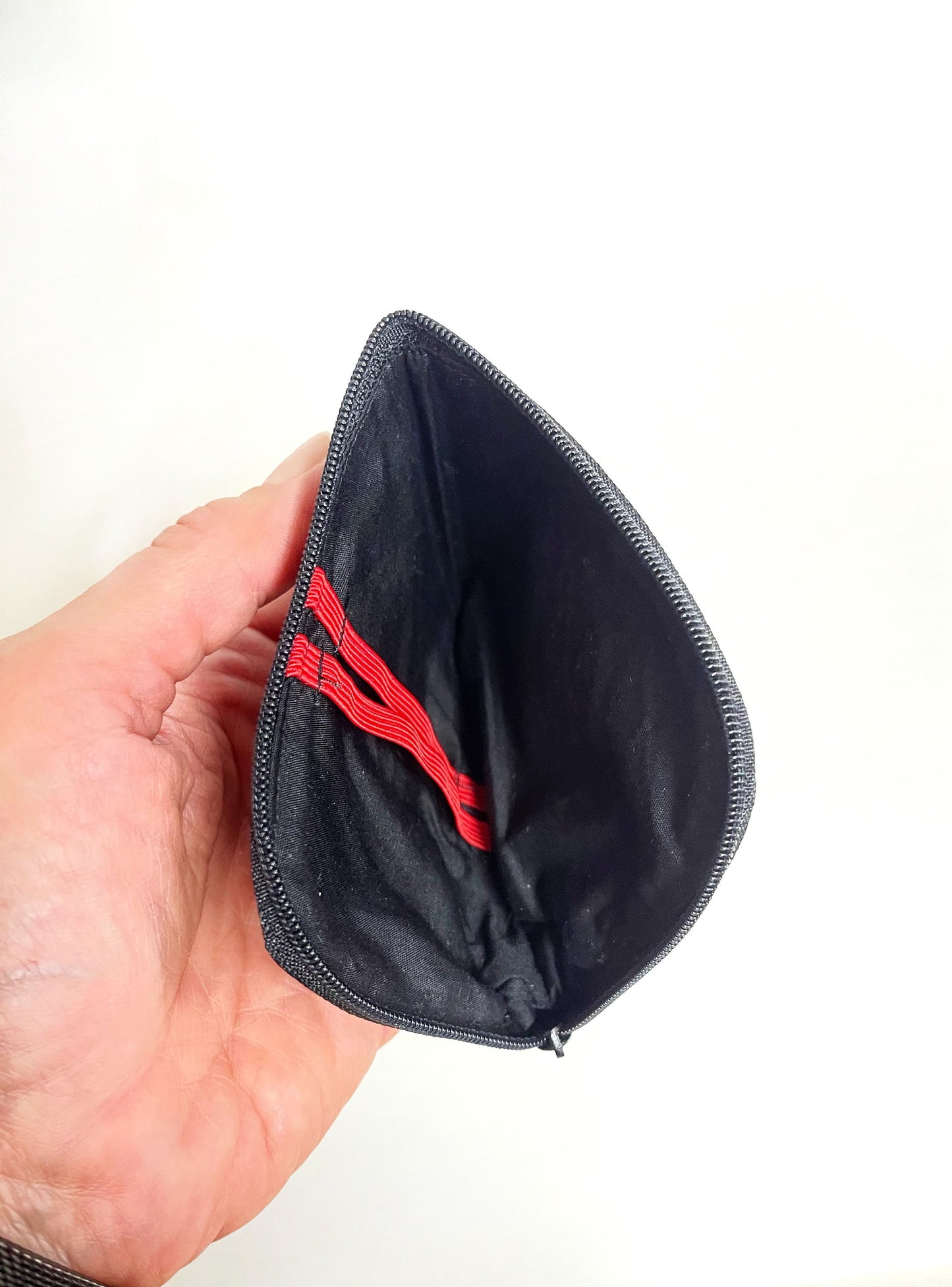 Eine Hand hält die geöffente Börse. Man schaut auf das schwarze Innenfutter und die roten Gummbänder. Die Börse ist leer. 