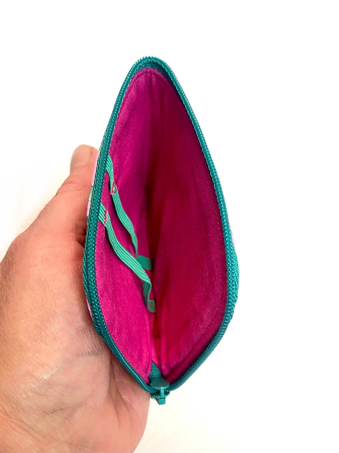 Eine Hand hält die geöffente Börse. Man schaut auf das pinke Innenfutter und die grünen Gummbänder. Die Börse ist leer. 