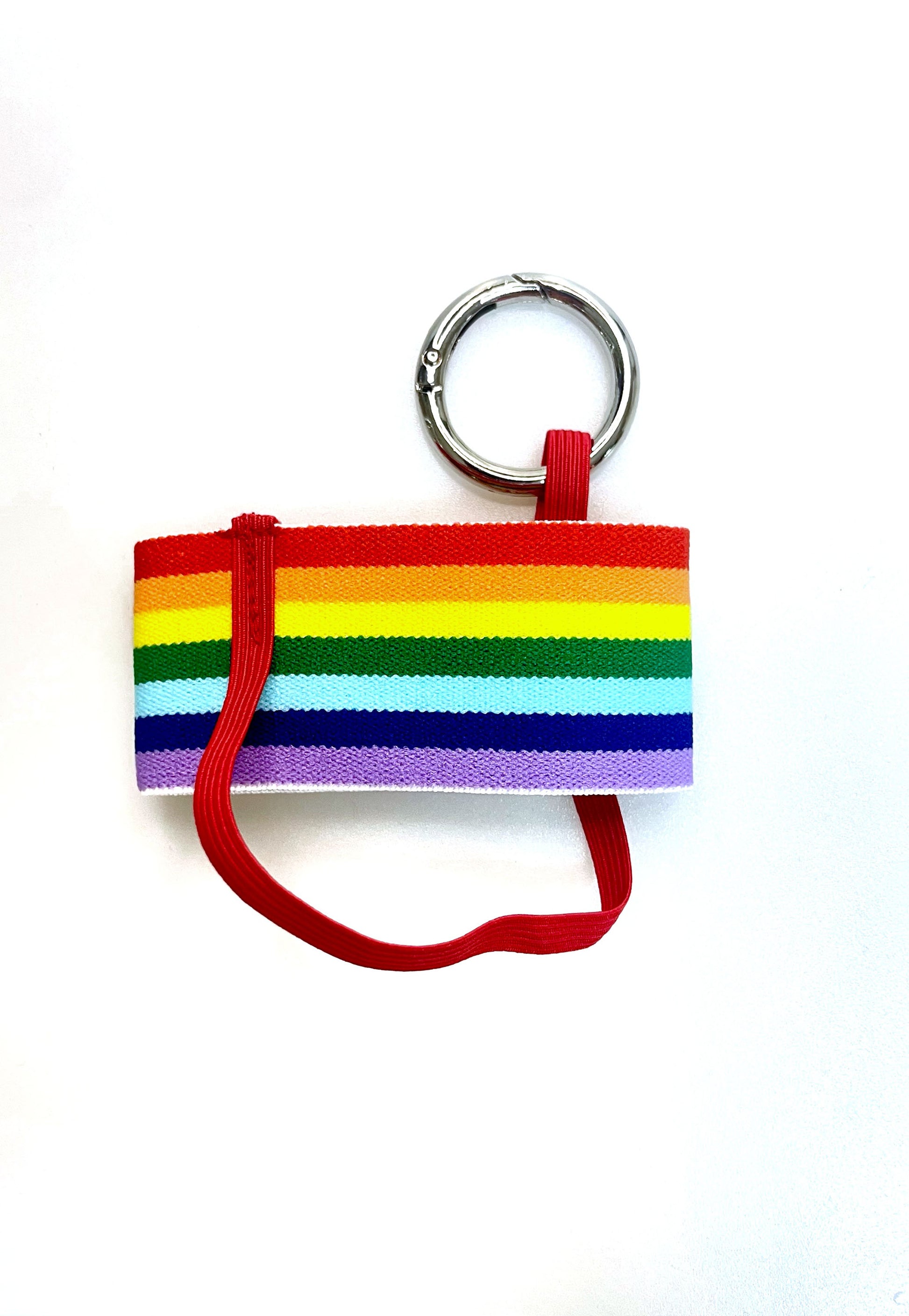 Der  Becherhalter mit den Regenbogen Streifen flach hingelegt. Man sieht, dass das schmale, rote Gummiband unten um den Halter herum geht. 