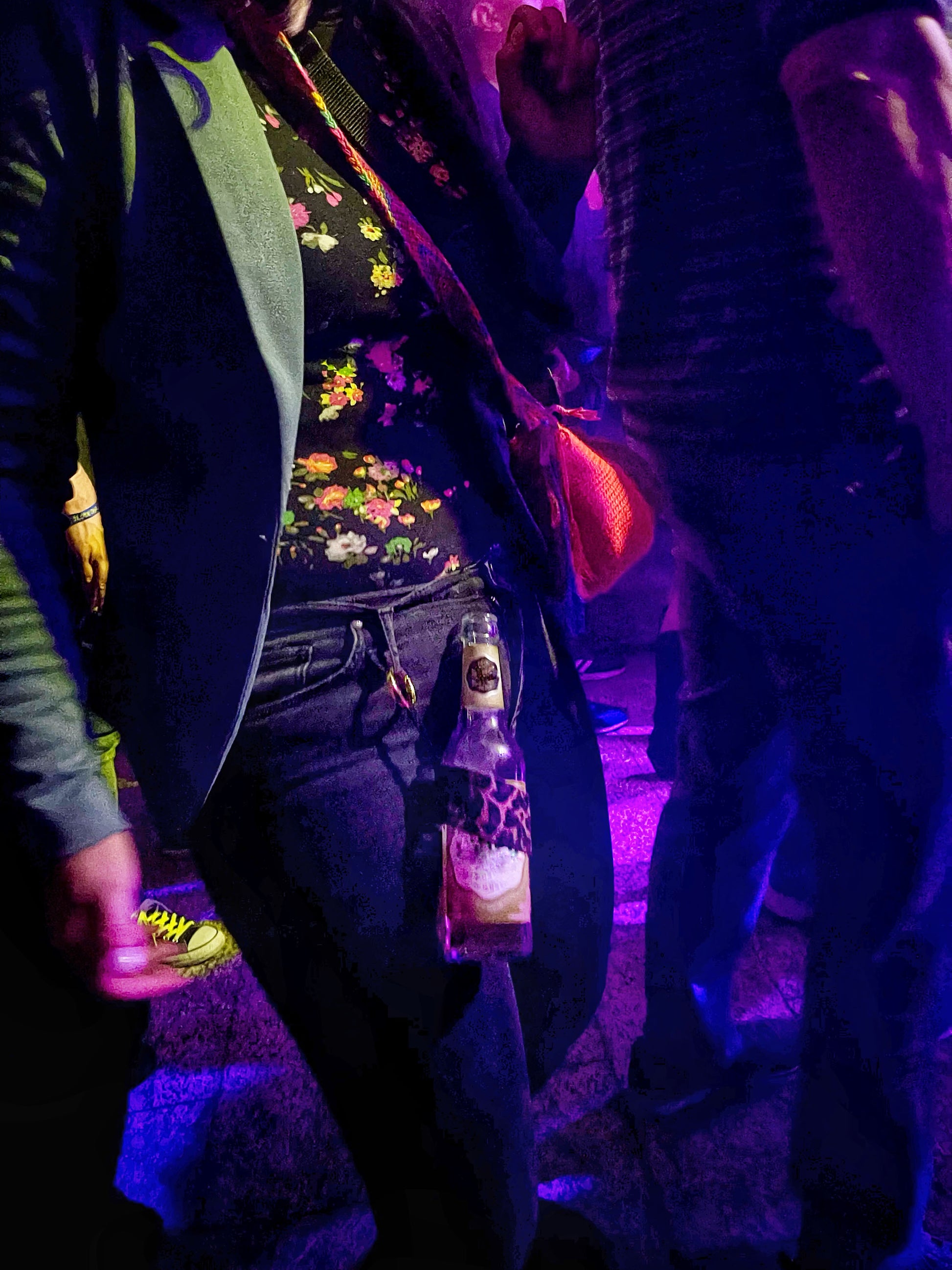 Der Becherhalter mit Leoparden Muster hängt an der Gürtelschlaufe einer tanzenden Frau in einem Club. Es steckt eine 0,33 Liter Flasche darin. Die Flasche ist etwa halb voll. 