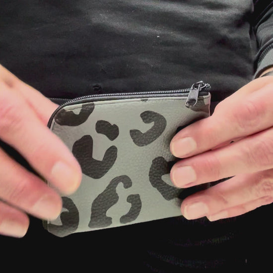 In dem Viedeo wird die graue Geldbörse mit den schwarzen Leopardenflecken geöffnet. Man sieht, wie der Reißverschluss auf und zu geht, wie die Aufteilung im Inneren ist und dass man an alles gut heran kommt.  