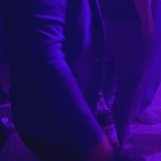 Der Becherhalter in Akrtion. Er hängt an der Gürtelschlaufe iner tanzenden Frau In einem Club. Es steckt eine 0,33 Liter Flasche darin. Die Flasche ist etwa halb voll. Im Lauf des Videos nimmt sie die Flasche aus dem Halter, trinkt und steckt sie wieder in den Halter. 