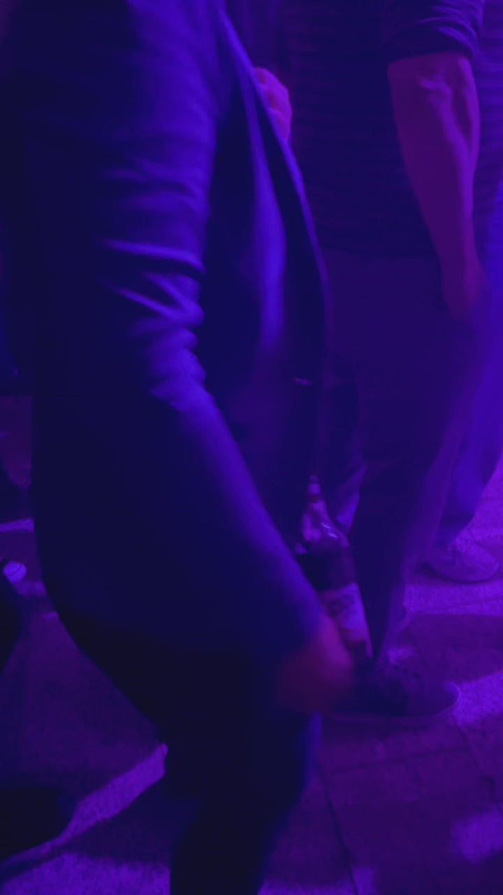 Der Becherhalter in Akrtion. Er hängt an der Gürtelschlaufe iner tanzenden Frau In einem Club. Es steckt eine 0,33 Liter Flasche darin. Die Flasche ist etwa halb voll. Im Lauf des Videos nimmt sie die Flasche aus dem Halter, trinkt und steckt sie wieder in den Halter. 